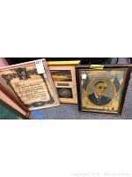 Three framed pieces displayed side-by-side on the floor including portraits and a signed award.