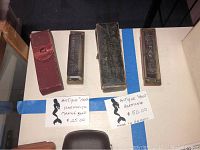 Four antique harmonicas and cases displayed on a white surface, including labeled price tags indicating age and origin.