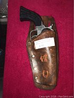 Vintage Pony Boy cap gun with black plastic handle inside the brown leather holster, showing embossed horse and horseshoe designs on holster.