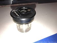 The ink well is shown from a side angle, highlighting the clear glass base and black Bakelite lid with swivel opening.