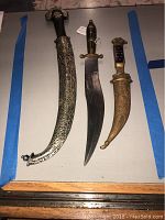 Full view of all three daggers on table showing detailed sheaths and handles.