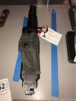 Top view of bayonet sheathed with green pouch and attached tag showing price and name.