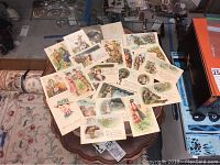 Wide arrangement of 24 colorful WWI remembrance cards featuring soldiers, couples, and patriotic themes placed on wooden table.