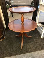 View of antique two-tiered wooden table with pie crust edges on top and bottom shelves, turned pedestal column, and tripod legs.