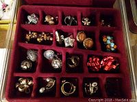 First image showing a red velvet organizer tray with 20 sections containing a variety of earrings and brooches of different styles and colors including metallic, faux pearls, and colorful stones.