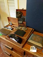 Overall arrangement of men's accessories showing wallets, sunglasses, jewelry boxes, and metal box on a wooden surface.