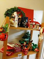 Photo of two wooden shelves displaying various Christmas decorations including fabric, plush toys, wreath, decorative boxes, and ornaments.