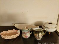 Five vintage porcelain dishes arranged on a shelf: a scalloped dish, an oval serving dish, covered sugar jar, floral creamer, and round covered bowl with gold trim.
