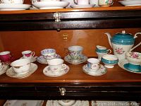 Wide view of tea cup and saucer assortment displayed inside a wooden cabinet.