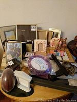 Collection of assorted picture frames of various sizes including plain, floral, and metallic frames along with additional accessories like mirror frames and stands on a wooden surface.