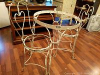 Wrought iron patio furniture set showing round table frame and two chair frames without seats, white paint with worn areas and patina.