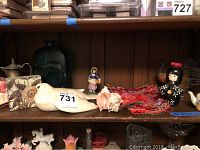 Shelf showing various decorative items including ceramic dove, wooden Asian figurine, colorful peacock, seashell, red fabric, and small ceramic teapot.