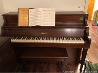 Front view of Yamaha upright piano with bench and open music book on rack.