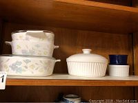 Three nesting Corning Ware floral pattern baking dishes and four other ceramic dishes including a ribbed white covered dish and two ramekins