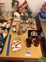 Photo shows various Christmas decorations including hand-painted eggs, angel figurines, bows, string lights, nativity set, and carved dog figurines arranged on a table.