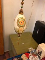 Photo of a handcrafted Christmas egg ornament showing a painted angel and child with beaded gold-tone top and bottom caps