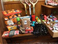 Photo showing plastic bowling set, tennis rackets, cards, pompoms, and stuffed animals on a wooden chest