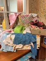 Photo showing folded baby doll clothes, blankets, and fabric items in pastel colors on a small sofa.