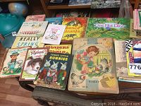 Full set of vintage children's books displayed on a table and a chair with some visible titles and cover art showing animals and children.