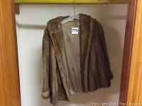Front view of the small brown mink fur jacket hanging on a hanger showing the fur texture and opening.