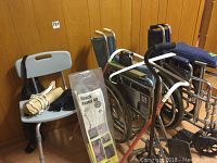 Photo of wheelchairs, shower chair, and boxed reach assist kit arranged against a wooden wall.