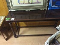 Vintage dark wood sofa table showing full length and turned carved legs with stretchers.