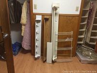 Five shelving units including four wooden white shelves with hooks of various sizes and one three-tier wire rack, arranged standing side-by-side against a wall.