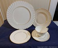 Full view of the place setting containing dinner plate, salad plate, bread and butter plate, cup, and saucer on a blue cloth background.
