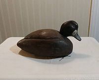 Side view of wooden duck decoy showing the detailed carving and painted finish in dark brown colors