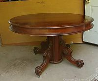 Full side and base view of the round walnut dining table showing carved legs and casters, split base design.