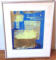 Framed abstract art print in blues and earth tones with white mat and silver frame.
