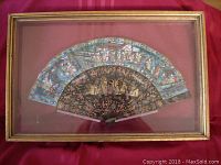 Frontal view of gilt wooden frame containing a hand-painted fan displayed with leaf fully open above carved black lacquer sticks.