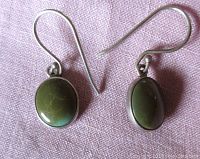 Front view of a pair of vintage oval green turquoise stone pierced earrings with silver hooks placed against a pink fabric background.