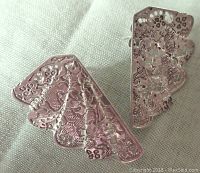 Close-up view of the front sides of the fan shaped sterling silver pierced earrings showing intricate floral and lace-like pierced and engraved details with scalloped edges.