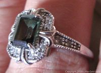 Front and top view of the ring showing the dark green emerald cut stone with decorative silver surrounding it and bead detail on the band sides.