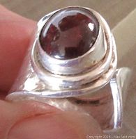 Close-up of the ring showing the red oval cabochon stone held by a silver bezel with hammered texture.