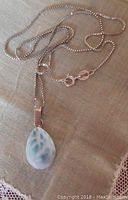 Photo of front side of the larimar pendant on the silver chain on beige fabric background