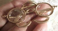 Front close-up photo of vintage gold tone eyeglasses brooch, showing round clear Lucite lenses and detailed coil nose pads.