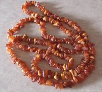 Long strand of Baltic amber chip beads in warm orange hues, laid on flat surface showing multiple loops.