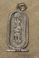Front view of sterling silver Egyptian cartouche pendant showing detailed hieroglyphics including a pharaoh head and scarab. Twisted rope frame and bail loop are visible.
