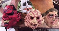 Four vintage adult latex Halloween masks laid on a wooden surface: red devil, clown, monster, human face.