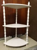 White painted wooden 3-tier corner knick knack shelf with spindle legs and finials, shown against brown background.