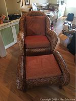 Front view of wicker armchair with cushion and matching ottoman with cushion on wooden floor.