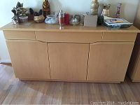 Front view of large wood buffet with three drawers on top and closed cabinet doors below, displaying various objects on top.