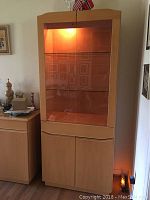 Front view of light wood china cabinet with glass doors and interior lighting on, showing upper display and lower storage sections.