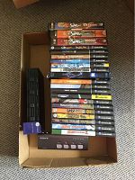All items laid out in cardboard box including DVDs and GameCube games with a black disc holder and black Sony device with pink buttons at bottom.