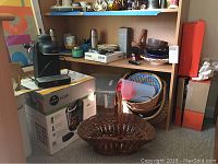 Picture showing Keurig coffee maker in box, black, Krups espresso machine, baskets stacked below shelf along with clear plastic container and paper products on shelf above.