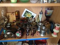 Wide view of various candle holders and souvenirs displayed on wooden shelves showcasing wood, metal, and glass materials.