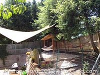 Sunshade attached and stretched over a backyard patio area with trees and house in the background.