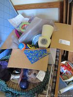 Photo showing open cardboard box with varied dog accessories including a loose ceramic food dish, toys, collars, and packaging material
